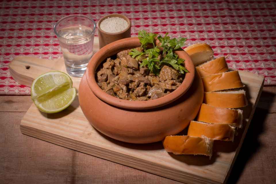 Miúdos de Galinha guisados, acompanhados de pão, farinha de mandioca e uma dose de cachaça.