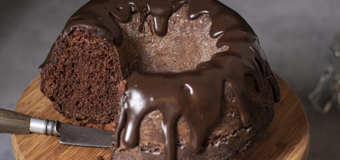 Um bolo de chocolate sem glúten cortado em fatia, sobre uma tábua de madeira, com calda de chocolate cremosa escorrendo