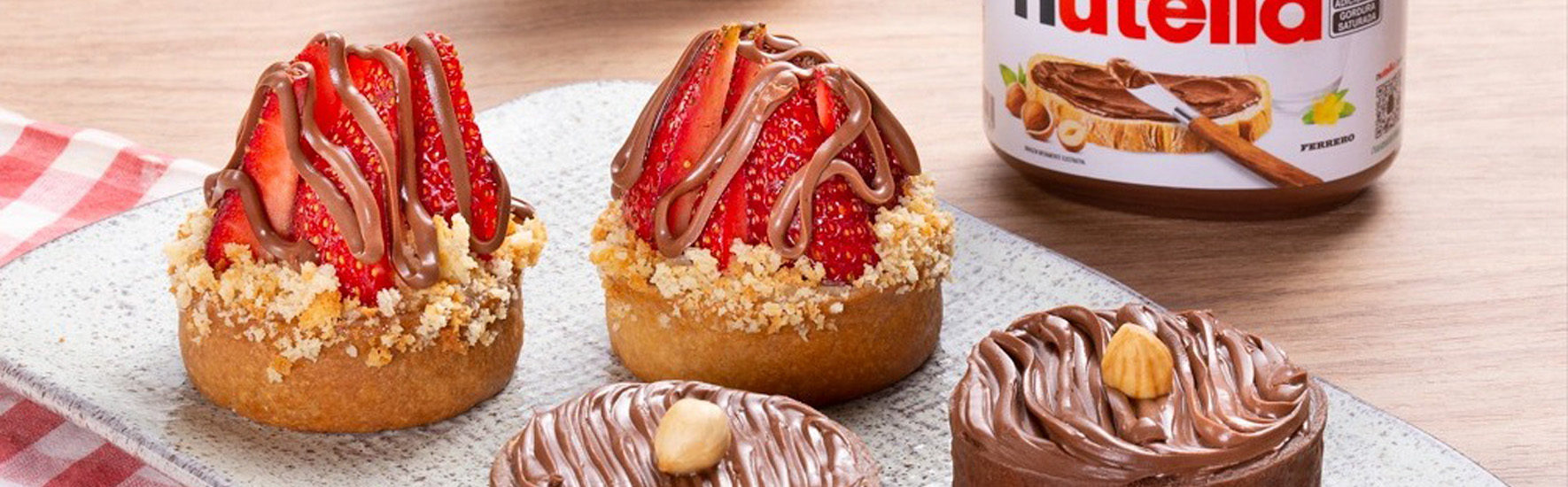 Uma foto que mostra uma variedade de docinhos feitos com Nutella, o creme de avelã e chocolate. Todos com uma aparência deliciosa e decorados com Nutella, morangos, avelãs, chocolate. A foto tem um fundo branco e uma iluminação suave, que destaca as cores e as texturas dos doces. A foto transmite uma sensação de doçura, tentação e sabor.