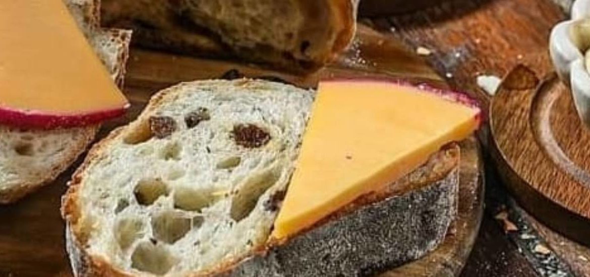 Pão fatiado e queijo em uma tábua de madeira, com uma tigela de molho ao lado.