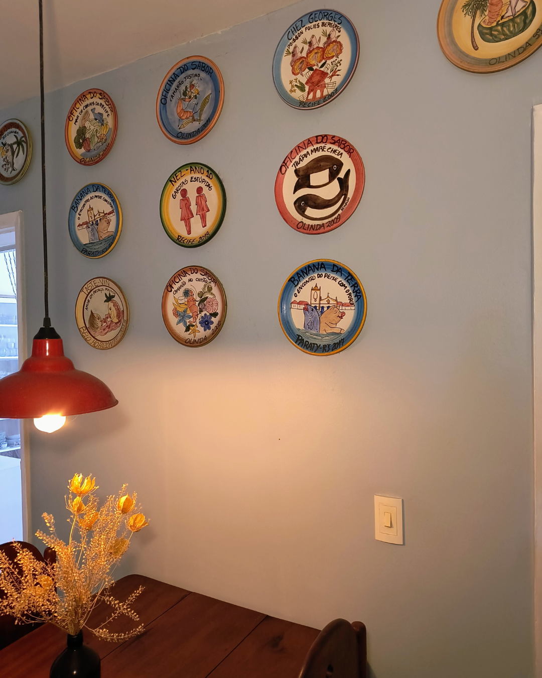 Luciana Torreão possui um mural de pratos da Boa Lembrança na parede da sala.